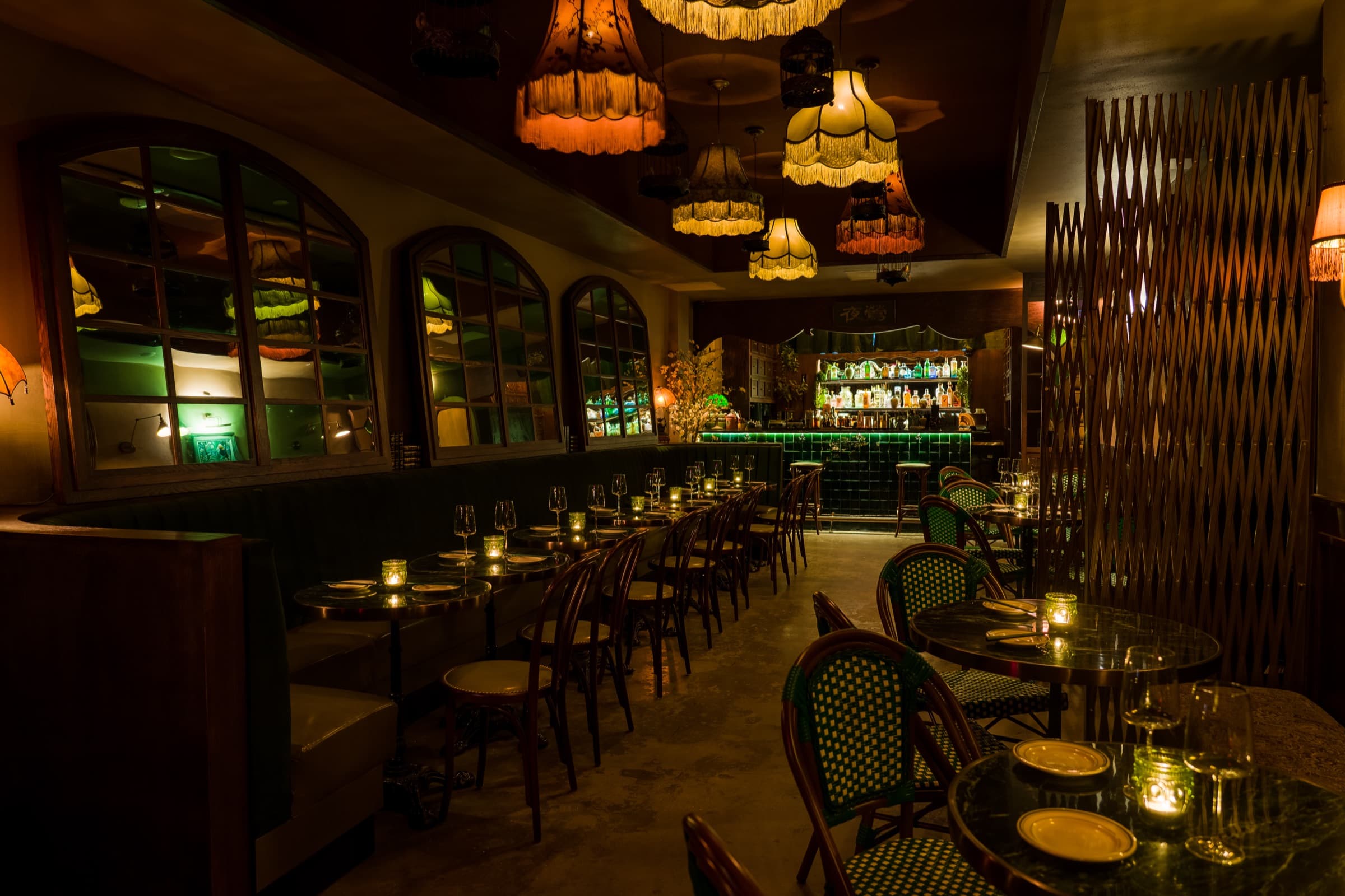 Ye's Apothecary dining room with vintage fringed lamps, arched green windows, and candlelit marble tables